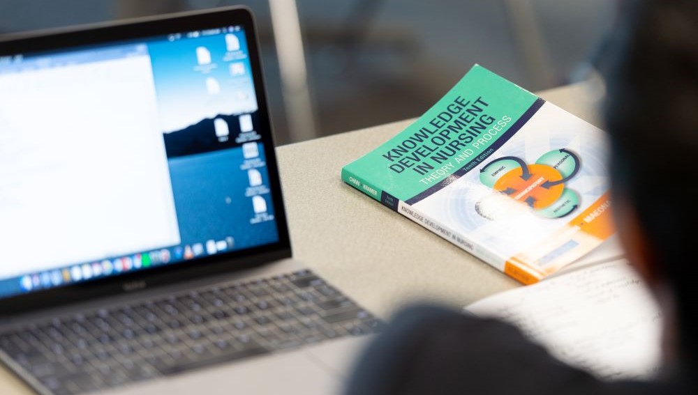 Laptop with nursing textbook next to it.